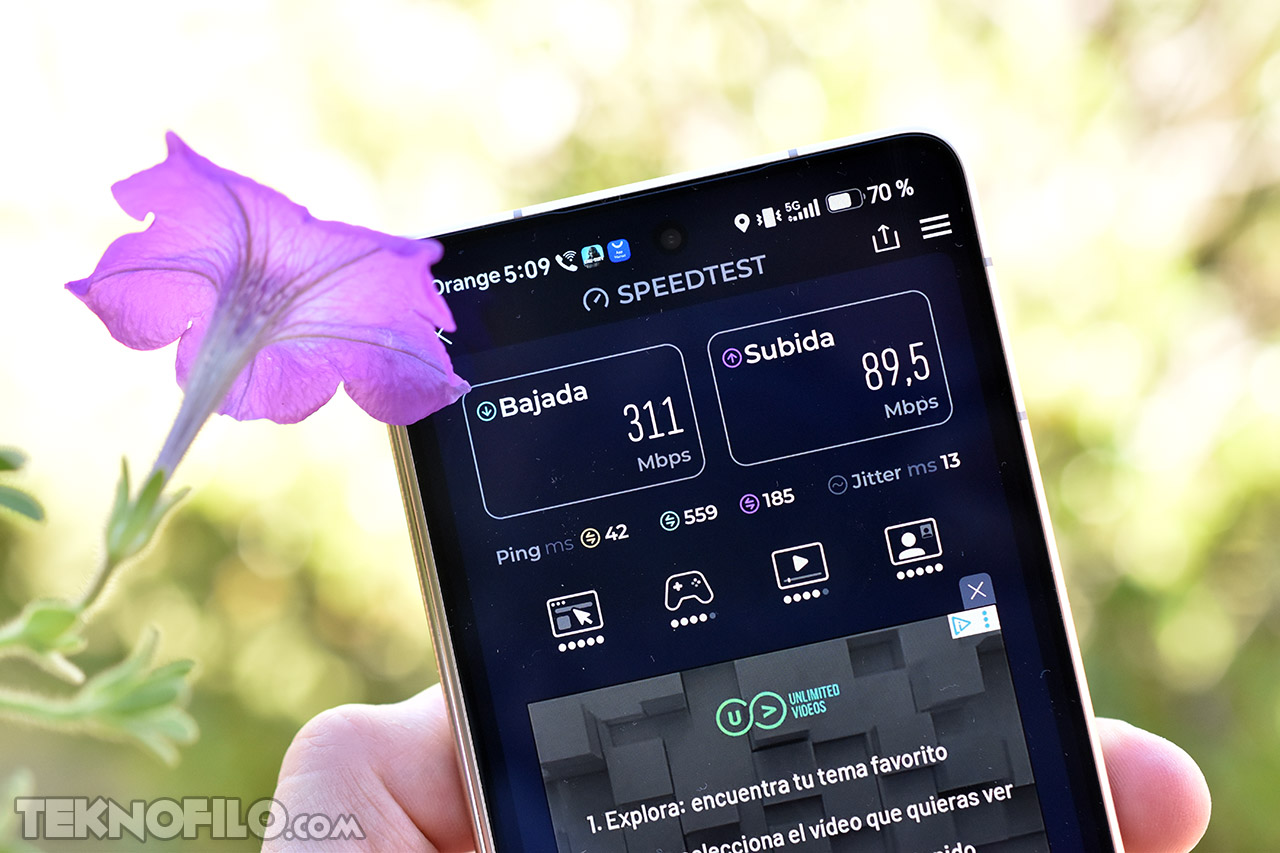 Prueba de velocidad de internet en smartphone, descarga 311 Mbps, subida 89.5 Mbps, junto a flor púrpura.