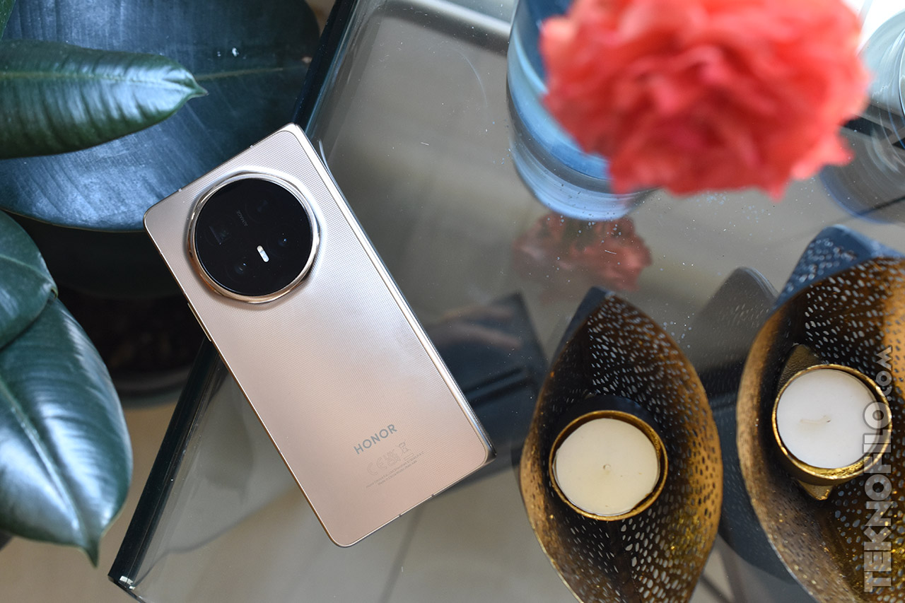 Smartphone Honor dorado sobre mesa de cristal con decoración de velas y planta.