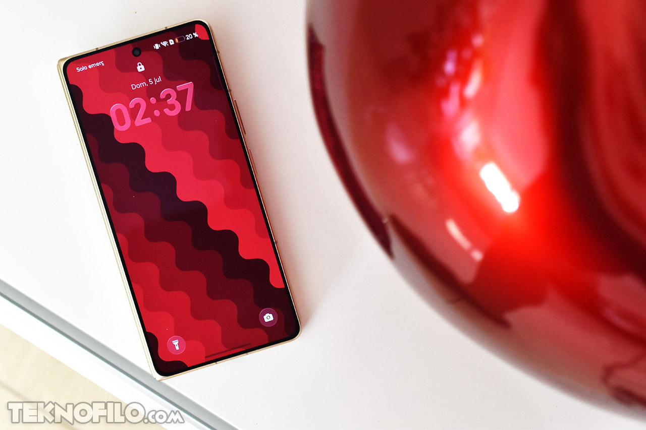 Smartphone con pantalla roja en la mesa, mostrando la hora 02:37, diseño de fondo ondulado.