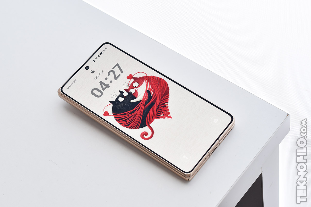 Smartphone plegable sobre mesa blanca mostrando pantalla de bloqueo con ilustración de gatos en diseño moderno.