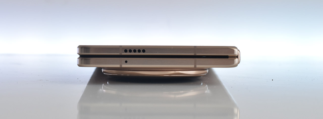 Smartphone dorado plegable cerrado visto de lado sobre una superficie blanca, mostrando su diseño delgado y moderno.