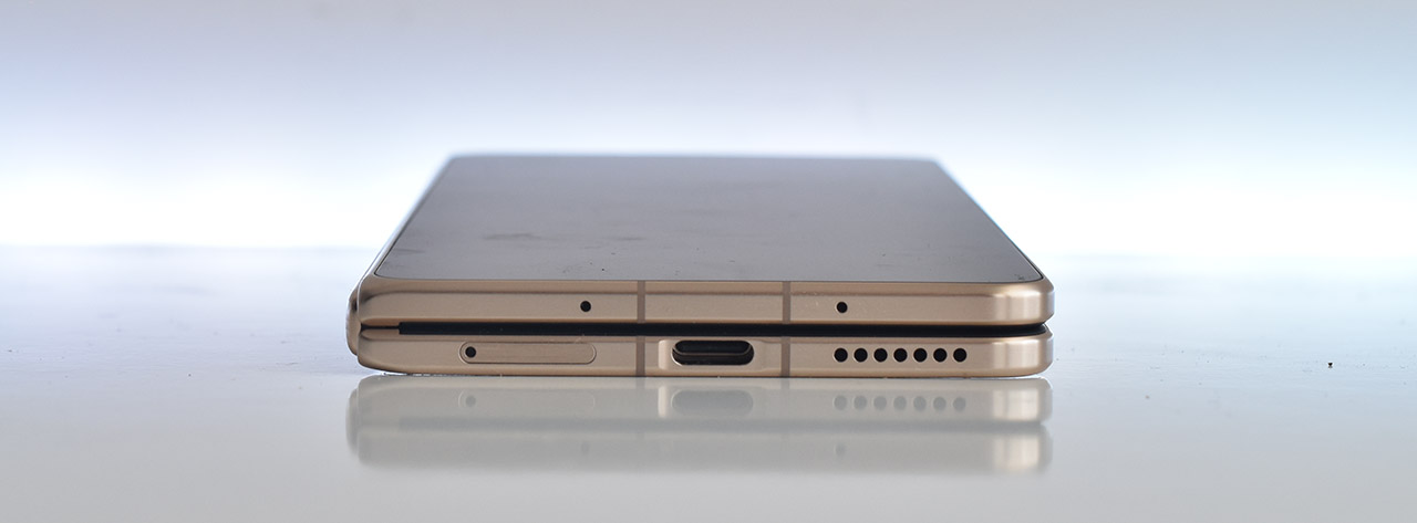 Teléfono inteligente plegado, vista lateral, color dorado, mostrando puerto USB-C y altavoz. Elegante diseño moderno.