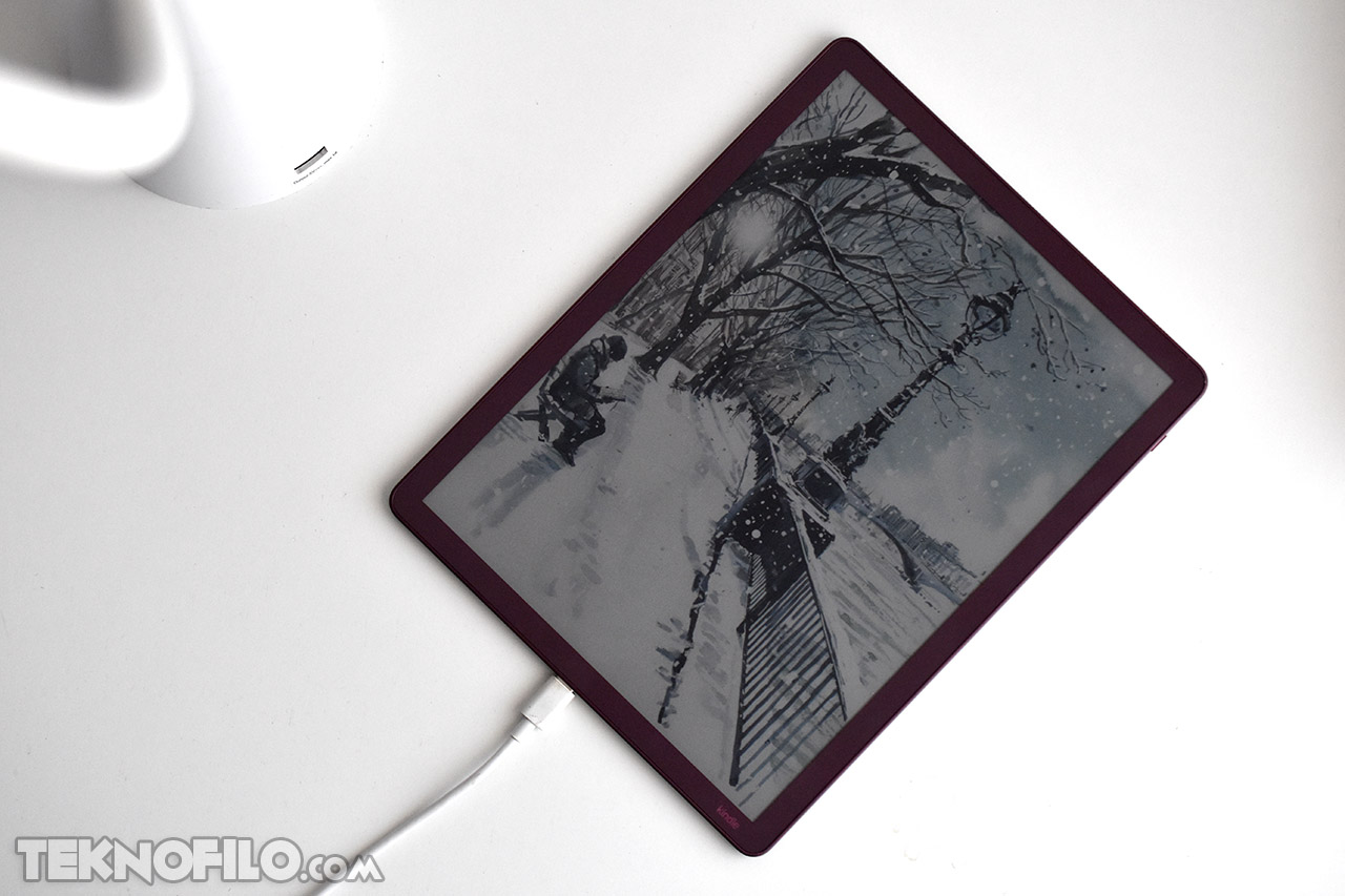 Tableta en carga con pantalla mostrando una escena de invierno nevada con árboles y persona caminando.
