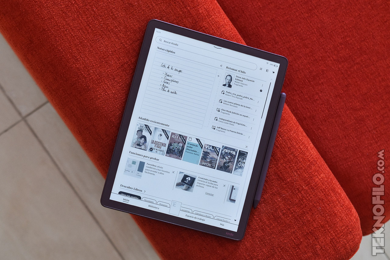 Tableta Kindle sobre un sofá rojo mostrando una lista de lectura digital y recomendaciones de libros en la pantalla.