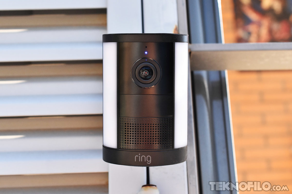 Análisis de la Ring Spotlight Cam de 2ª gen.: más detalle y libertad sin cables Cámara de seguridad inteligente Ring montada en una pared, con lente y micrófono visibles para vigilancia del hogar.