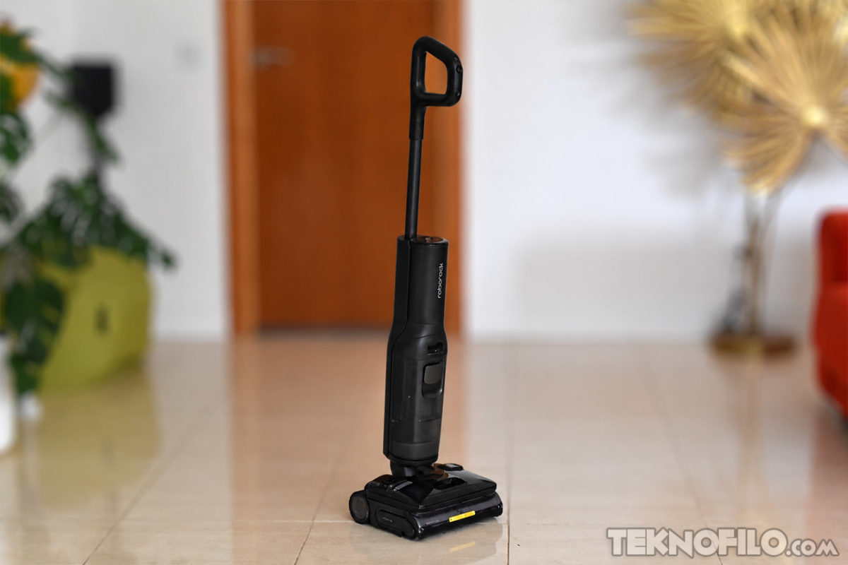 Análisis y opinión de la aspiradora Roborock F25 Steam con vapor de agua Escoba eléctrica negra en el suelo de una sala moderna con plantas verdes y muebles de fondo.