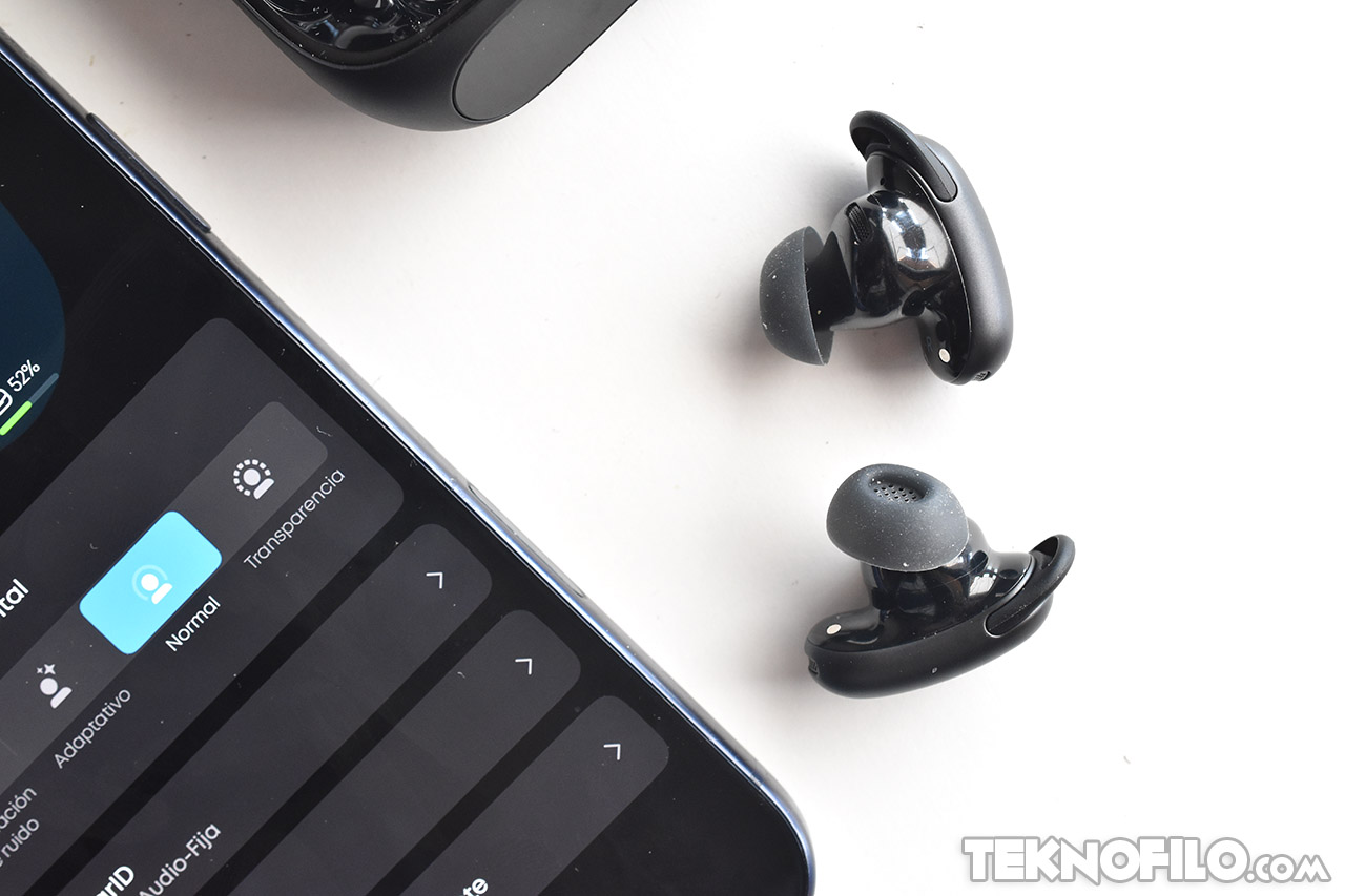 Auriculares inalámbricos negros junto a un teléfono mostrando opciones de audio.