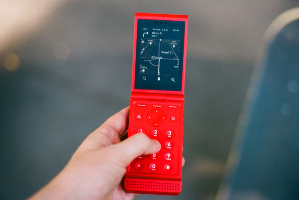 Light Flip recupera el móvil de concha para ayudarte a dejar las redes sociales Teléfono plegable rojo con pantalla GPS encendida, sostenido en una mano para navegación.