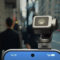 Cámara montada en smartphone 5G en una calle urbana, personas caminando al fondo, tecnología moderna.