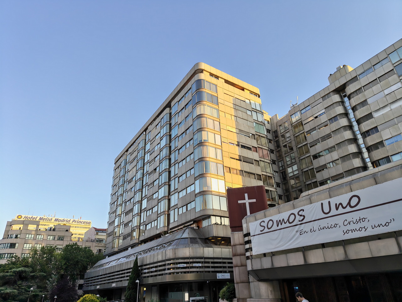 Edificio moderno en Madrid con letrero religioso y vista al hotel Meliá Madrid Princesa al fondo.