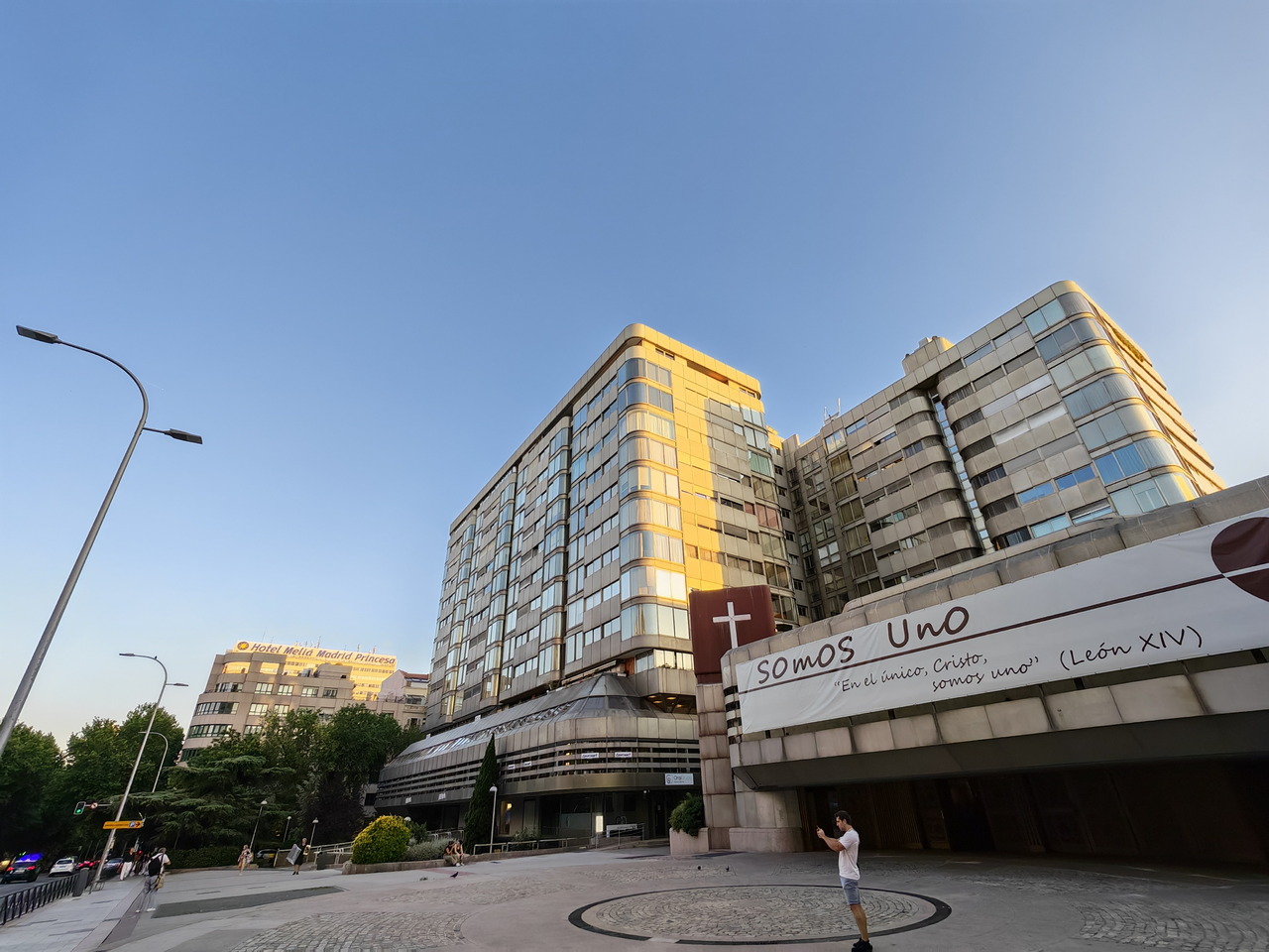 Fachada del edificio con cartel Somos Uno, cielo despejado y peatones caminando al atardecer.