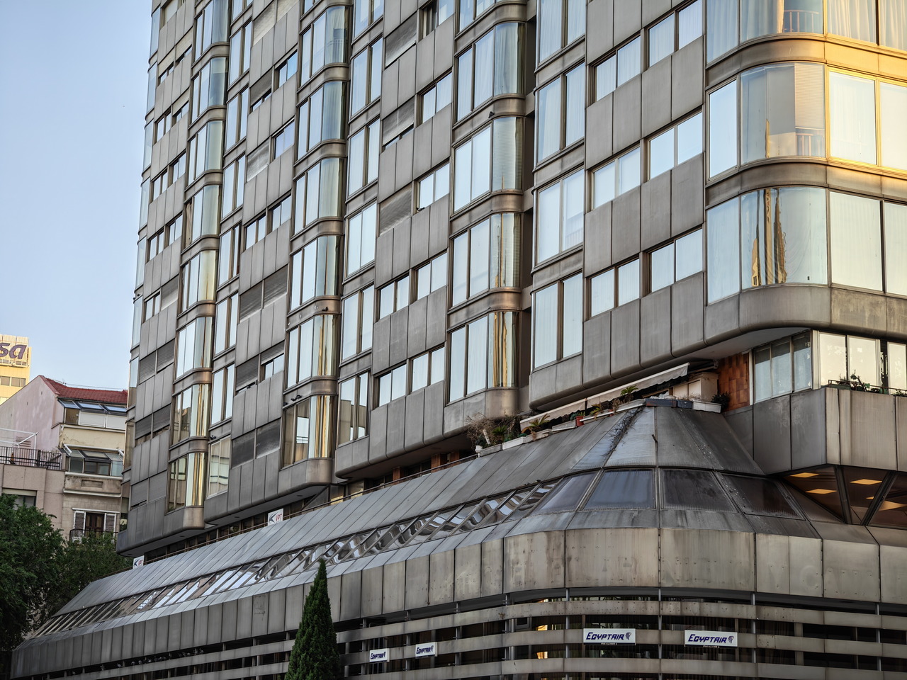 Edificio moderno con fachada de vidrio y metal en una calle urbana al atardecer.