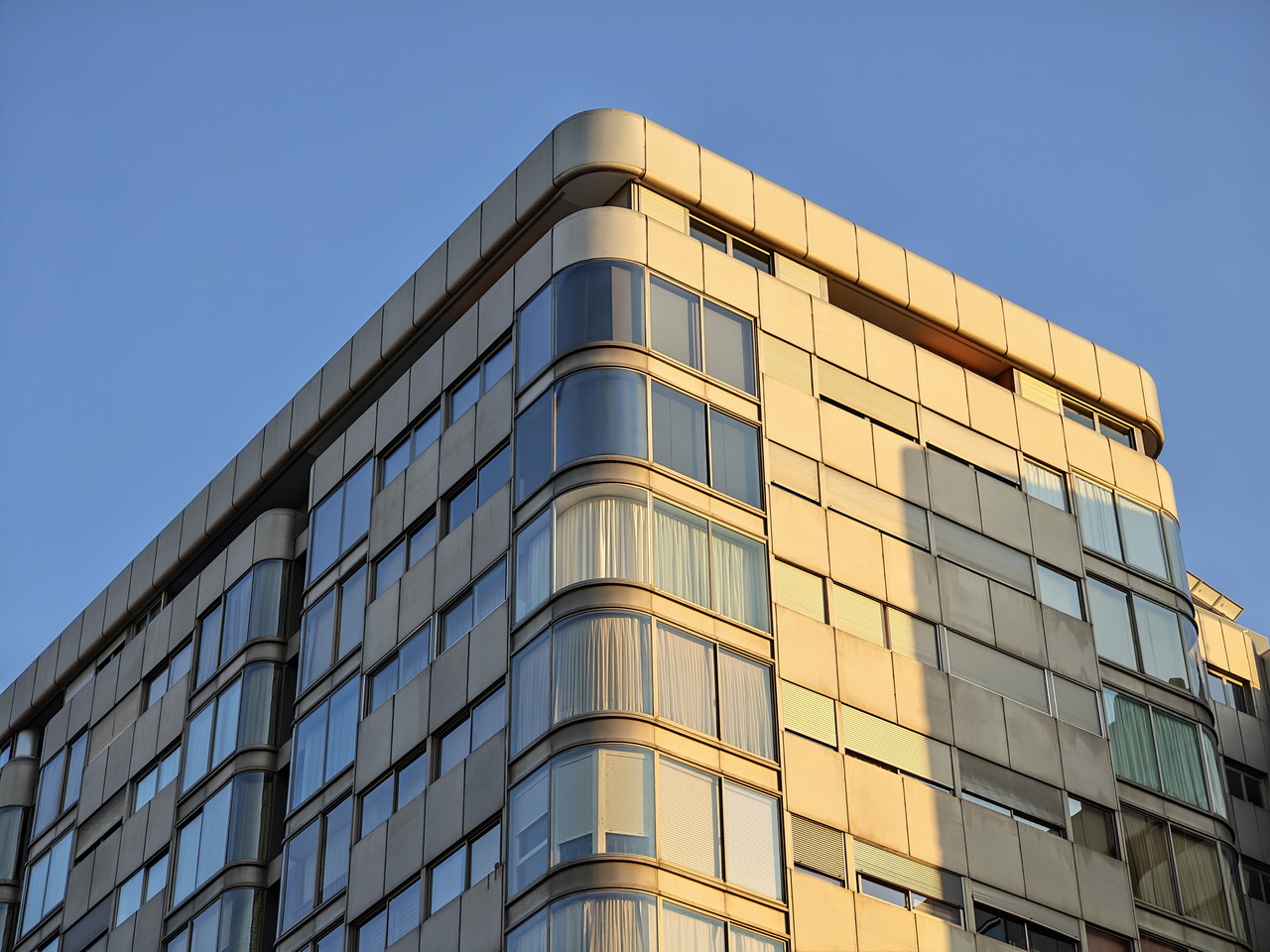Edificio moderno con ventanas reflectantes al atardecer, cielo azul claro de fondo.