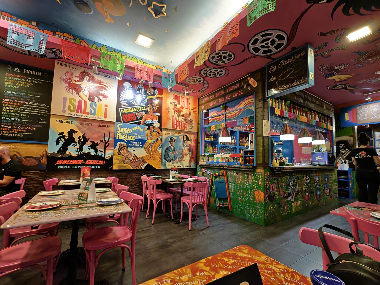 Restaurante mexicano colorido con carteles vintage, mesas rosas y papel picado decorativo en las paredes.