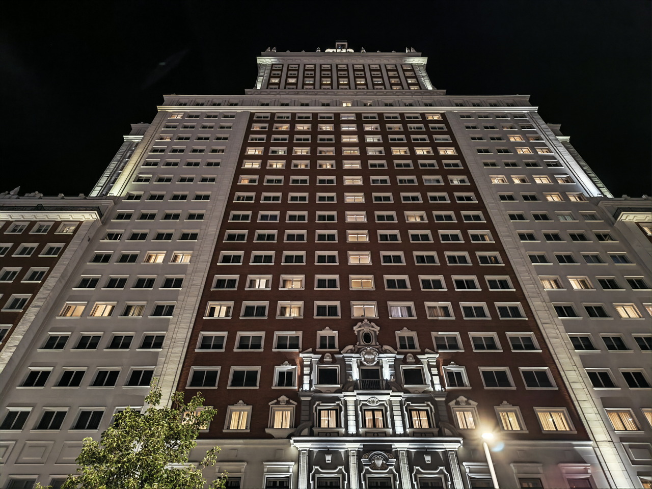 Edificio de gran altura iluminado por la noche, visto desde abajo, con fachada clásica y ventanas alineadas.