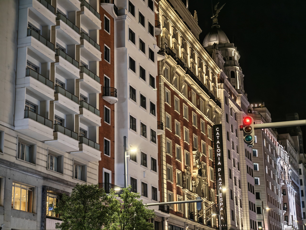 Edificios iluminados en la Gran Vía de Madrid por la noche, con semáforo en rojo al frente.
