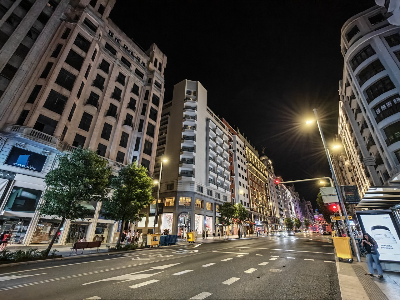 Avenida iluminada de noche en Madrid, con edificios y tiendas vibrantes, ideal para pasear y disfrutar.