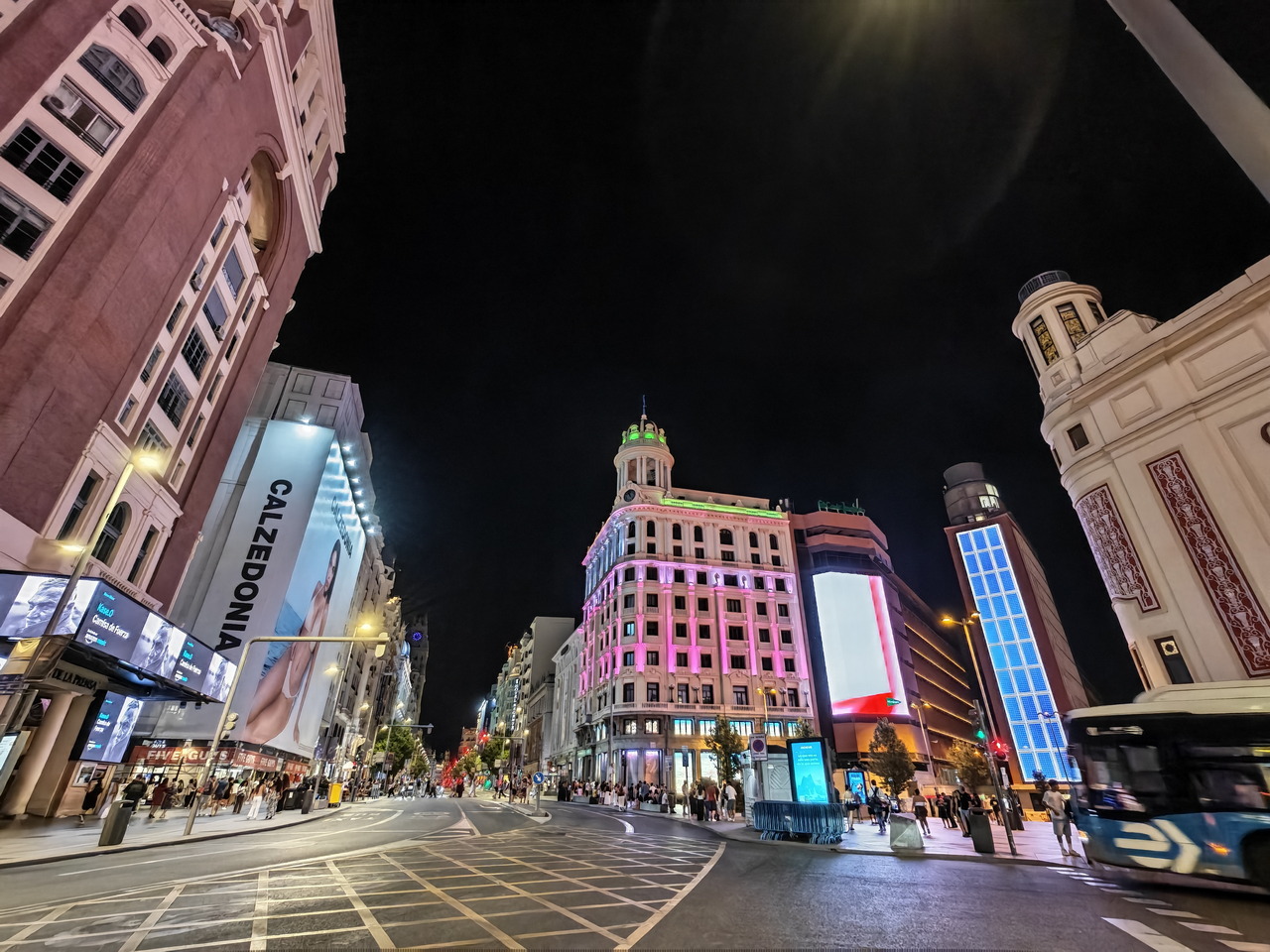 Calle Gran Vía de Madrid iluminada por la noche con edificios y luces coloridas.