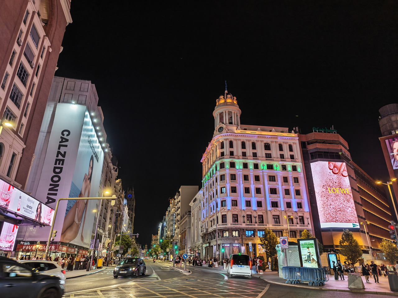 Calle de Madrid iluminada de noche con edificios y carteles publicitarios brillantes.