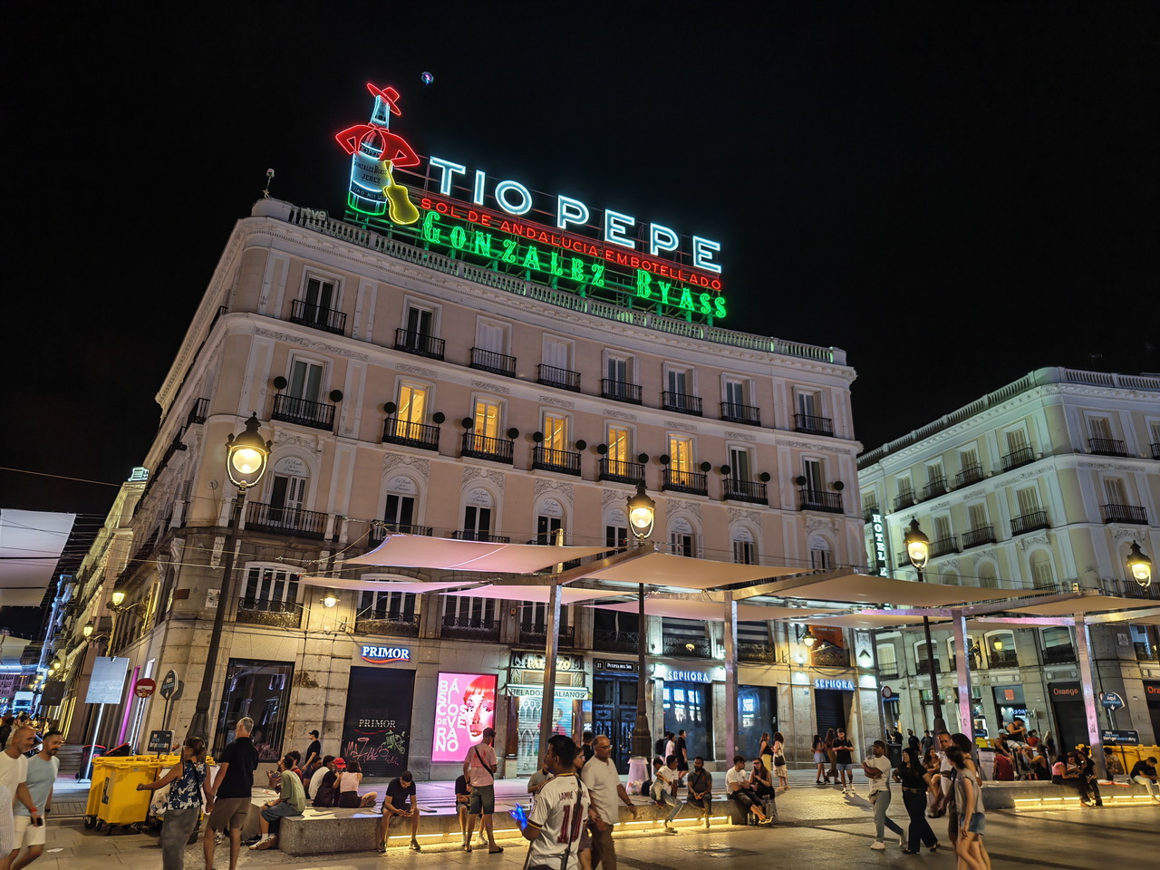 Edificio iluminado con cartel de Tío Pepe en la Puerta del Sol, Madrid, de noche. Personas paseando y descansando.
