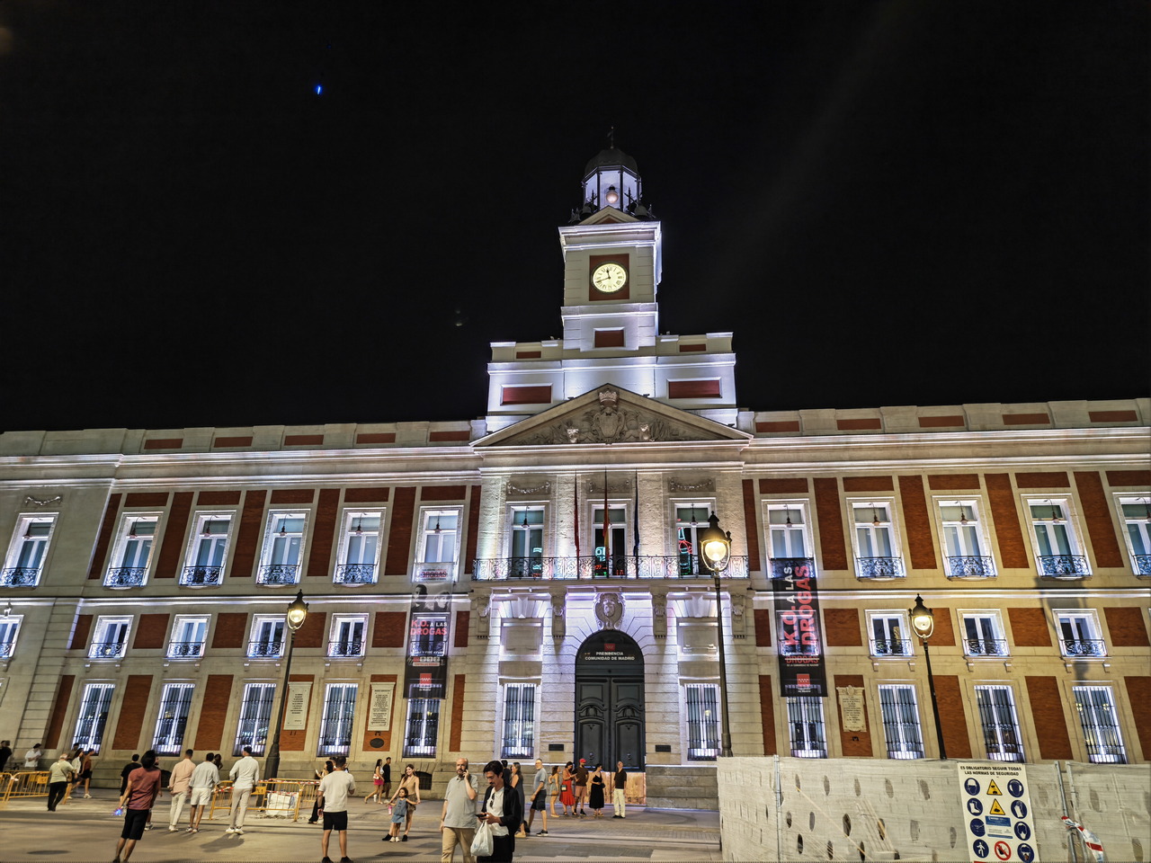 Edificio iluminado en la Plaza Puerta del Sol, Madrid, de noche con gente paseando.