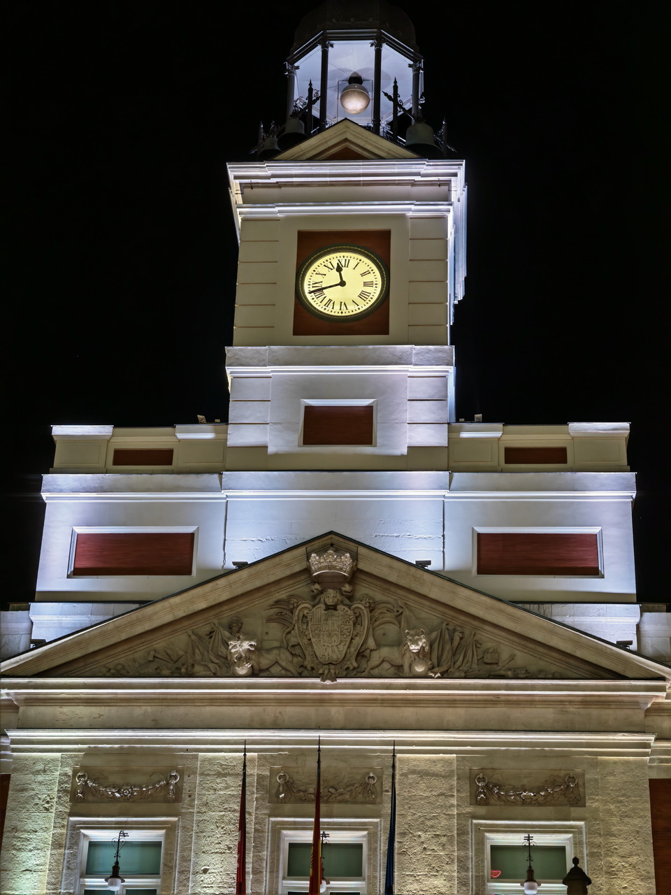 Reloj iluminado de la Puerta del Sol en Madrid por la noche, destacando su arquitectura histórica.