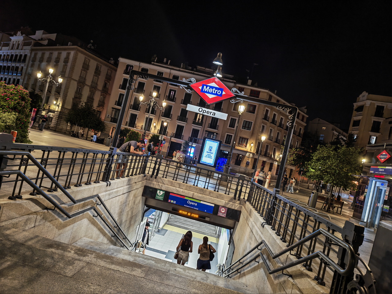 Entrada al metro de Ópera en Madrid por la noche, con luces de calle y edificios alrededor.