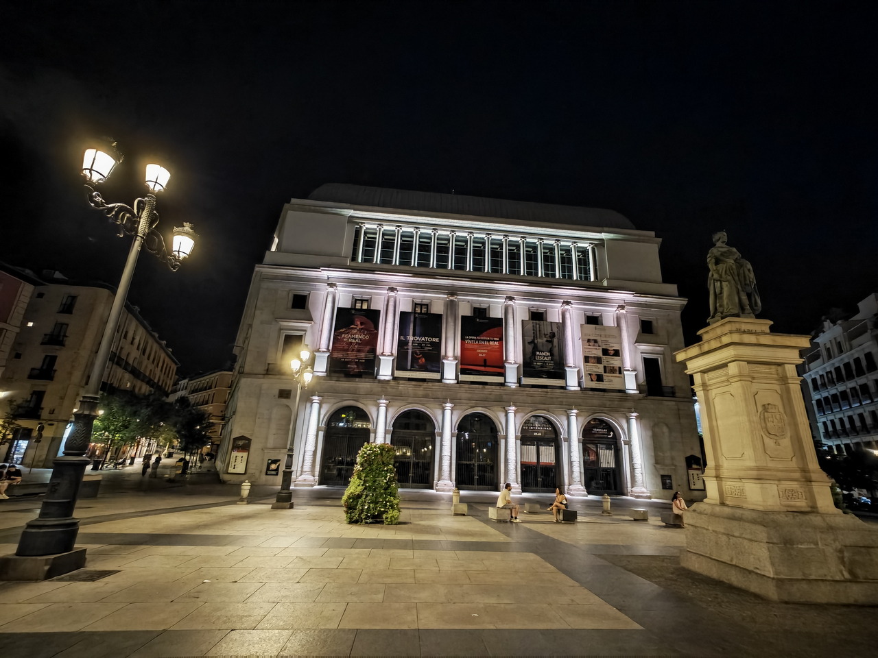 Teatro Real de Madrid iluminado de noche, con una estatua en la plaza y farolas encendidas.