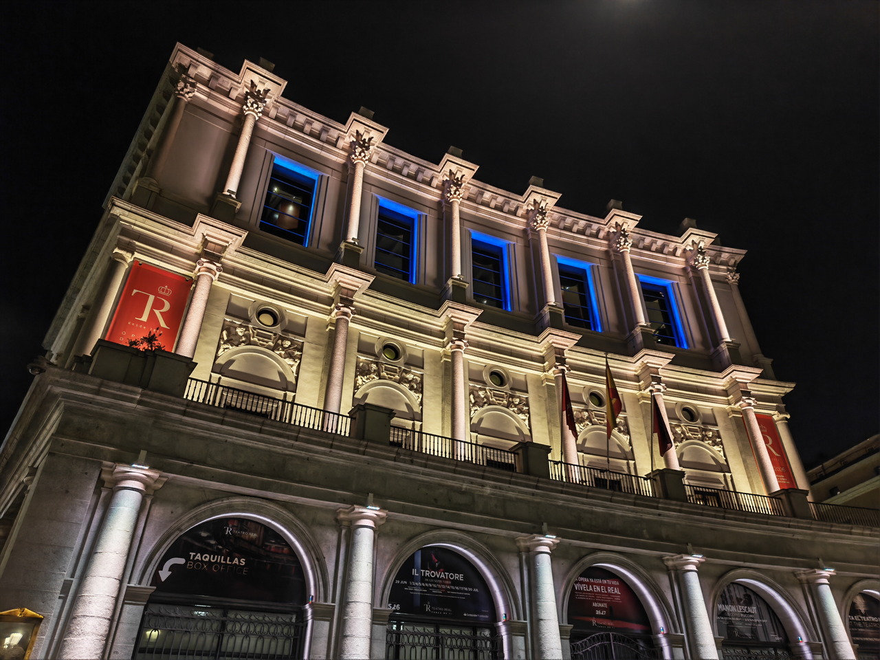 Fachada iluminada del Teatro Real por la noche en Madrid, con detalles arquitectónicos a la vista.
