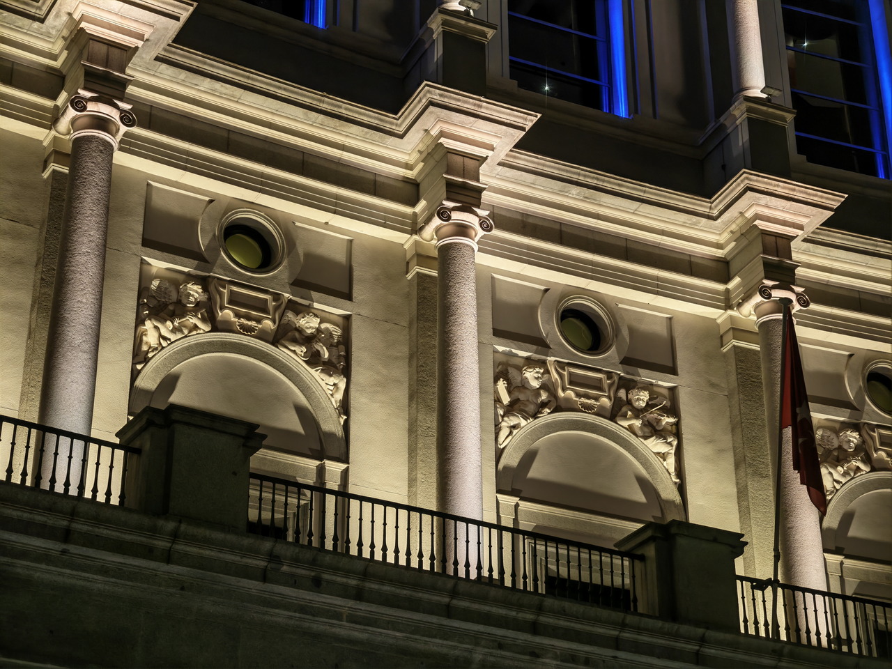 Fachada iluminada de un edificio histórico con detalles arquitectónicos, columnas y esculturas decorativas.