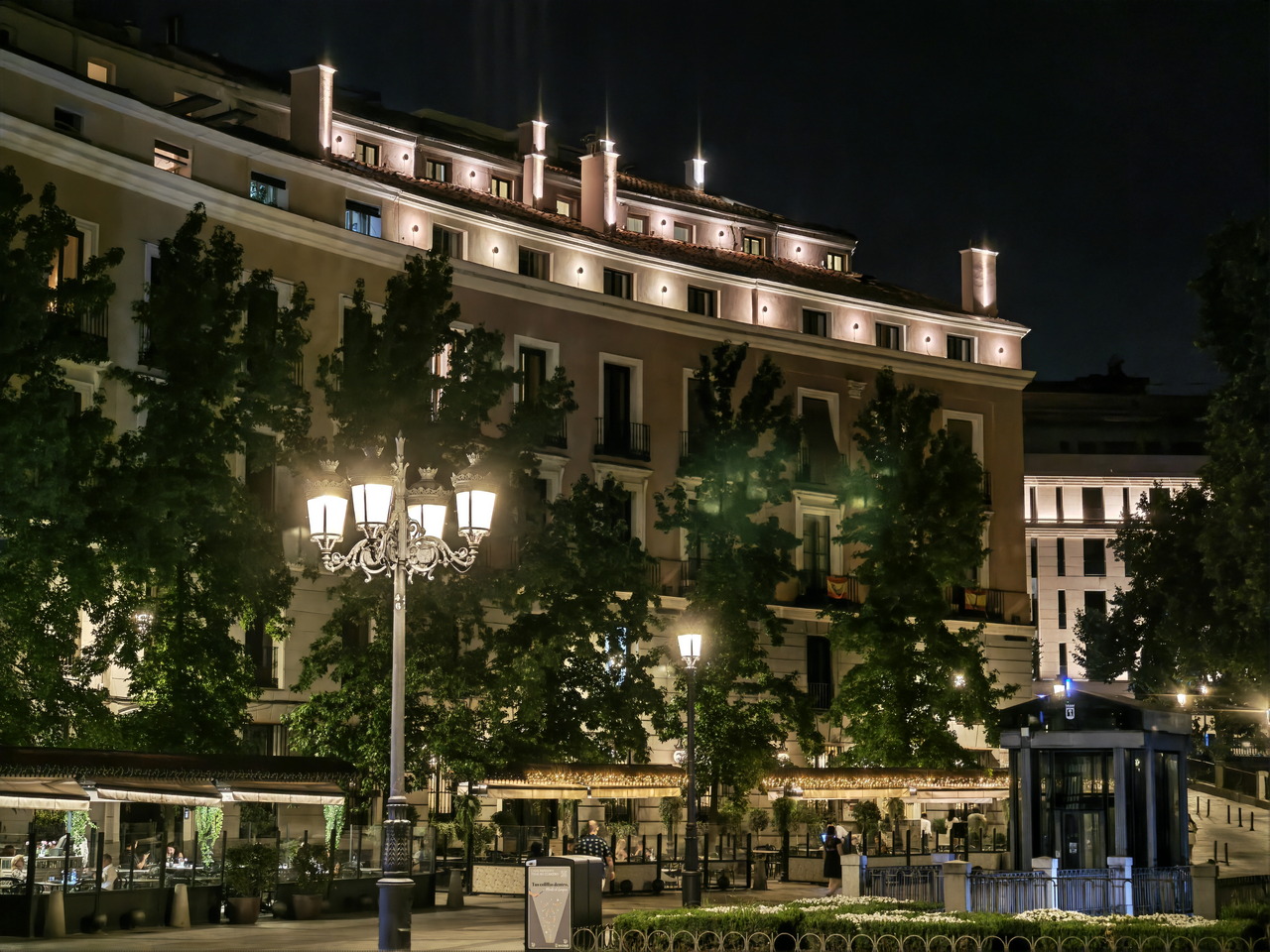 Edificio iluminado de noche en una plaza con faroles y árboles, creando un ambiente tranquilo en la ciudad.