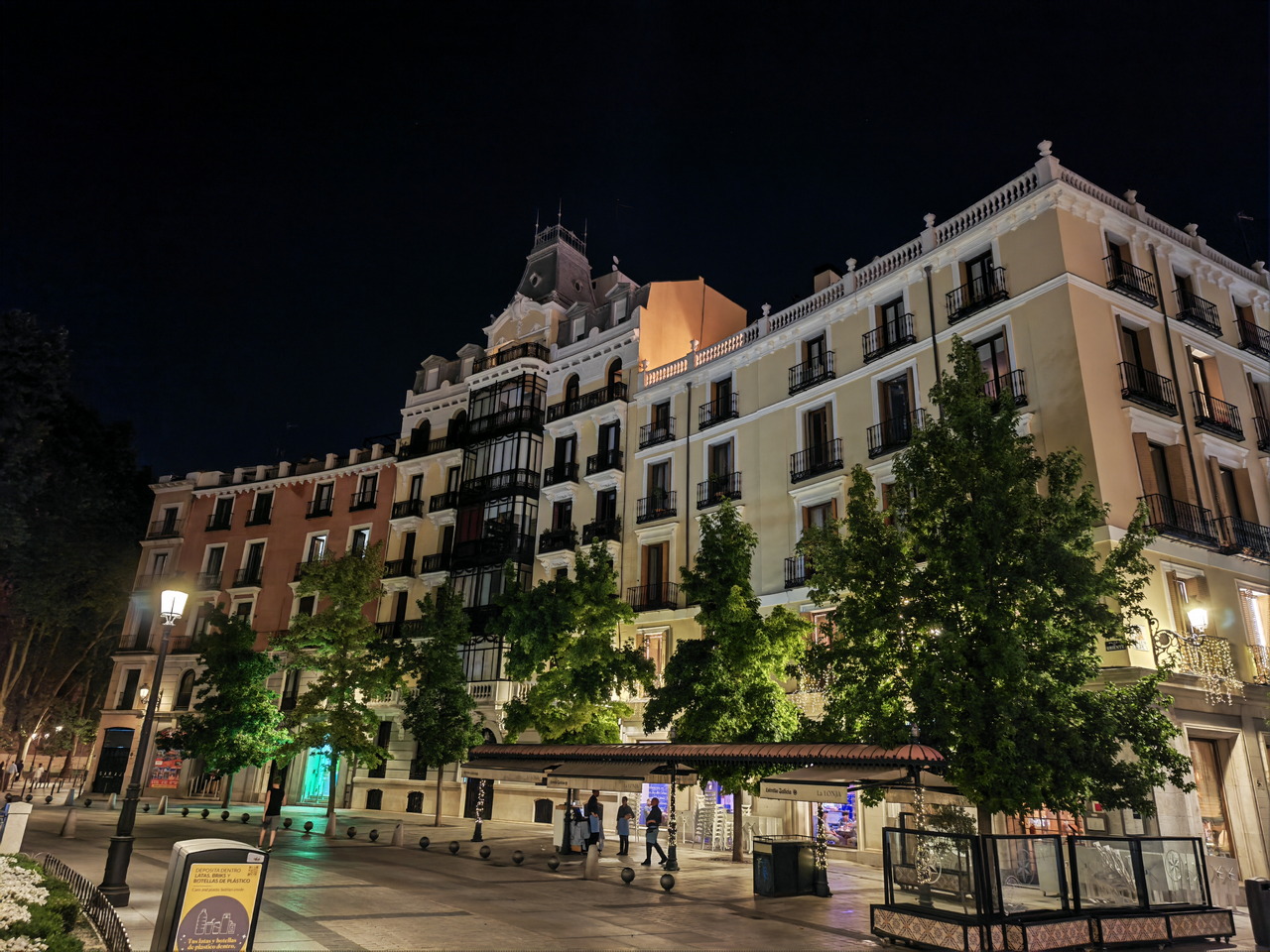 Edificio iluminado en una plaza nocturna con árboles y farolas en Madrid. Arquitectura histórica y ambiente nocturno.