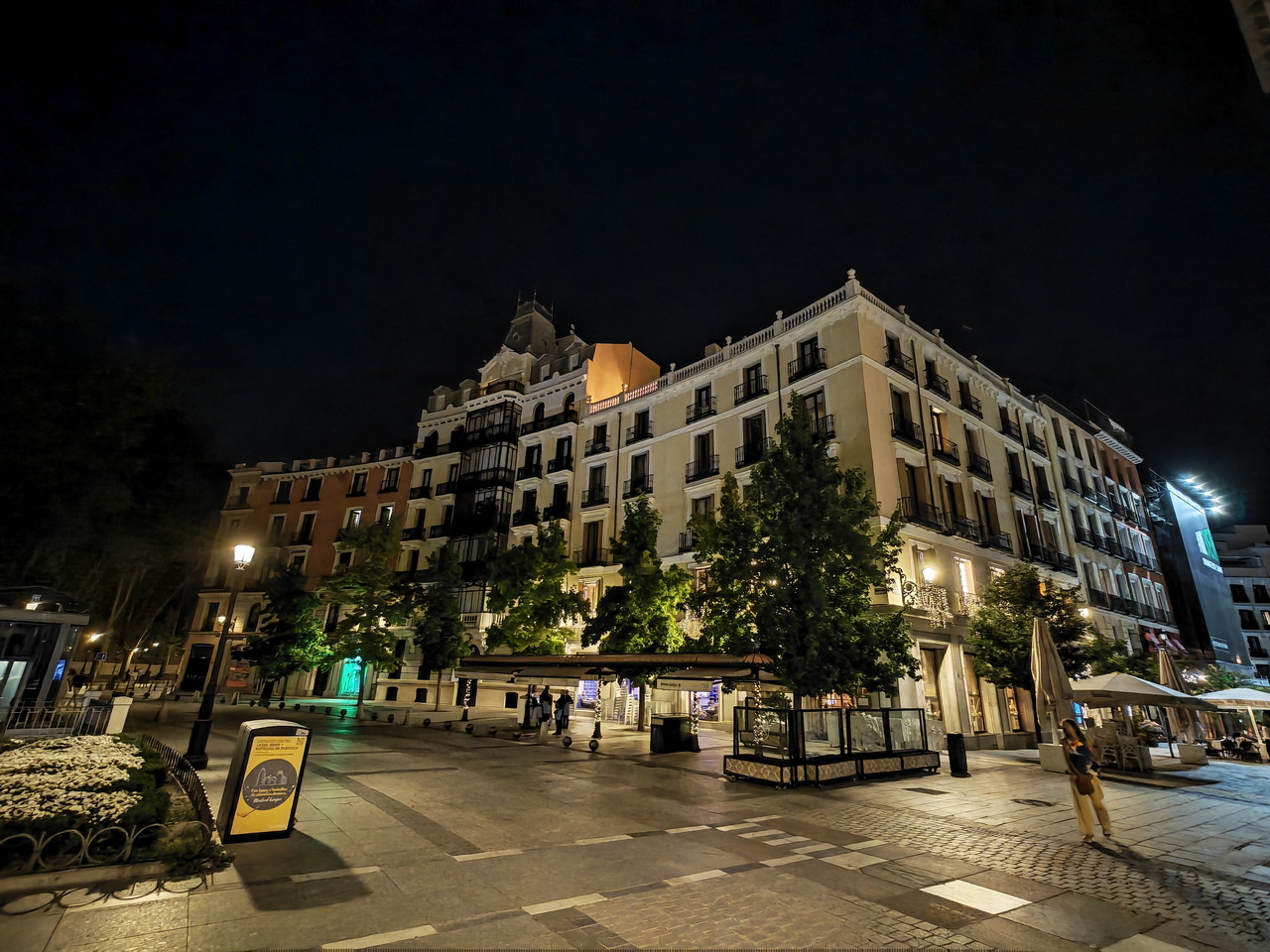 Plaza iluminada por la noche en Madrid, con edificios históricos y árboles, ambiente tranquilo y nocturno.