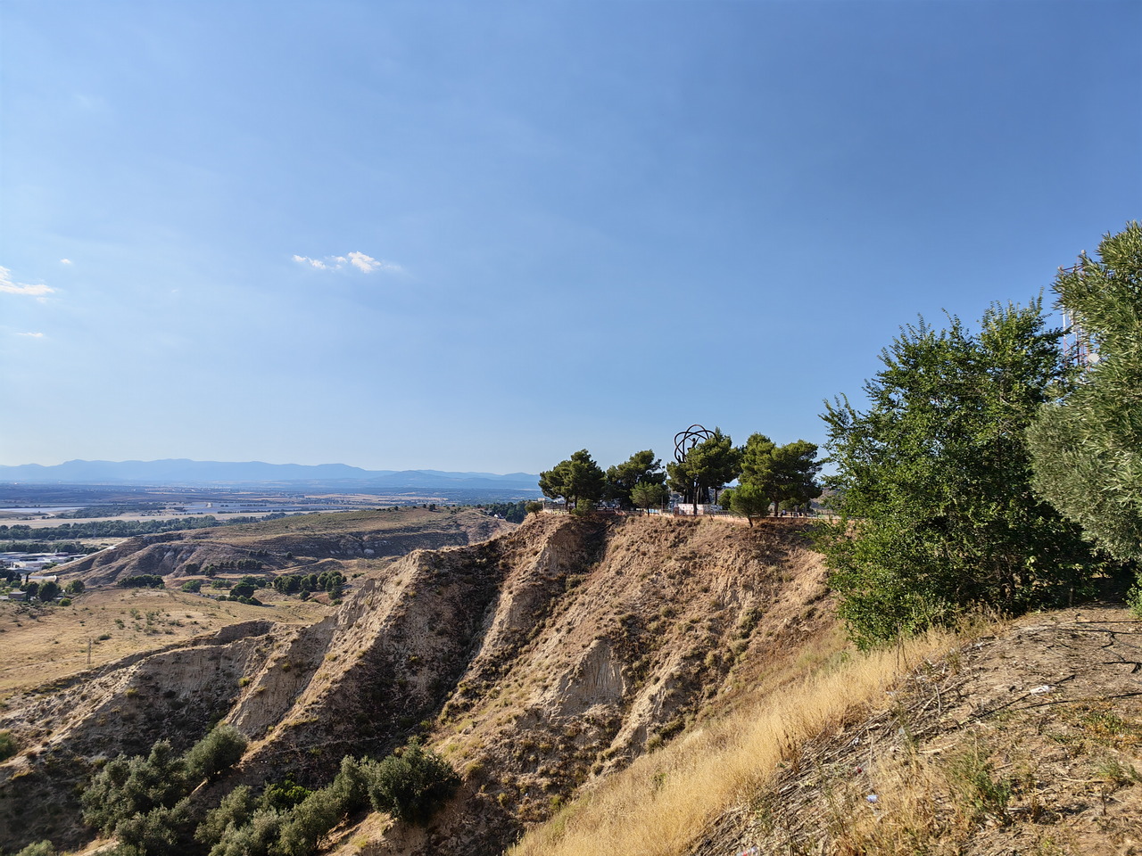 Vista panorámica de un paisaje seco con colinas, árboles y cielo despejado en el horizonte.