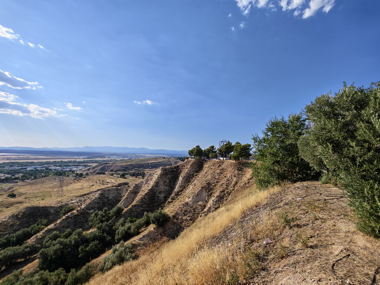 Vista panorámica del paisaje rural con cerros y árboles bajo un cielo despejado en un día soleado.