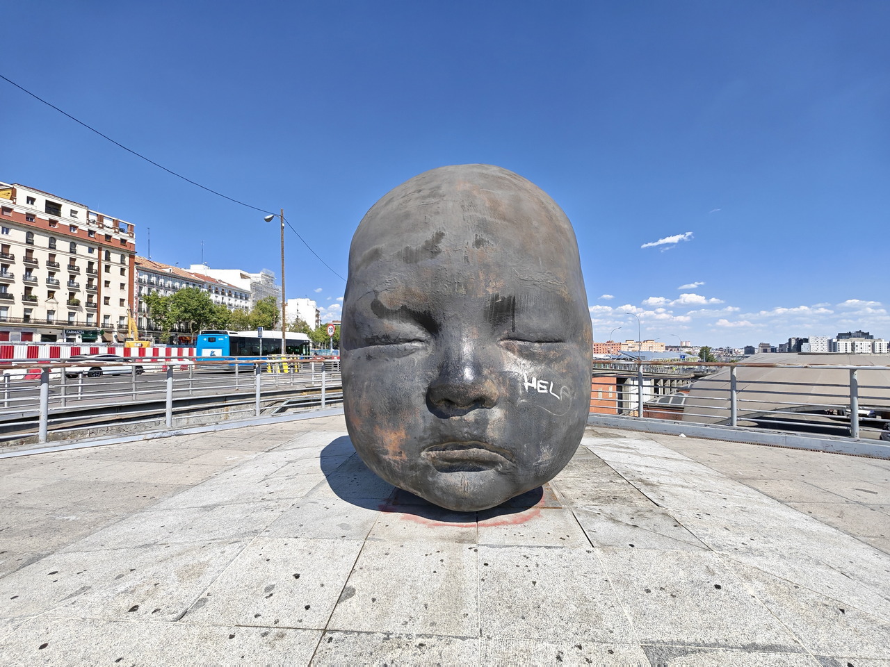 Escultura de cabeza de bebé grande en un puente de Madrid bajo un cielo azul despejado.