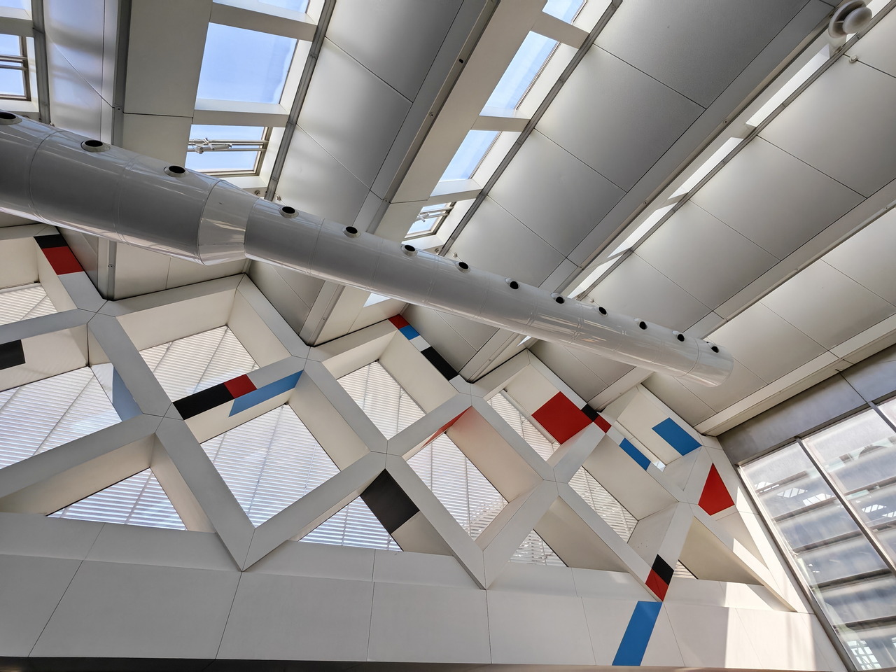Techo interior moderno con diseño geométrico y ventanales grandes, estructura colorida y luz natural abundante.
