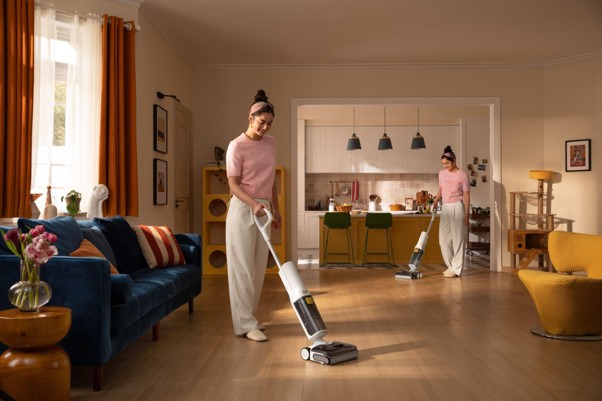 Roborock lanza las F25 Steam y F25 GT Gen 2: aspiración, fregado y vapor Persona usando aspiradora en sala moderna con cocina al fondo, muebles coloridos y decoración acogedora.