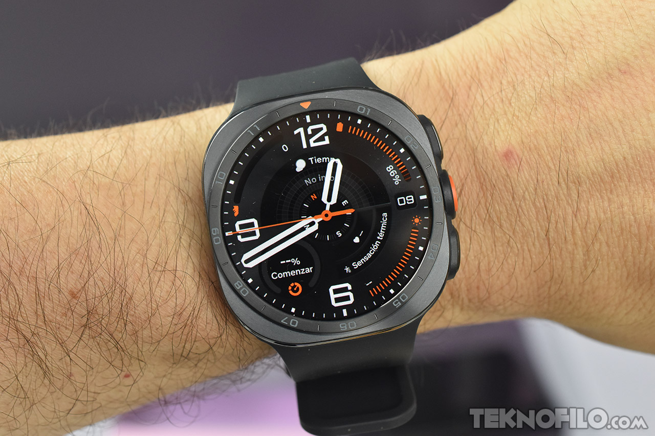 Reloj inteligente negro en muñeca mostrando hora y funciones. Pantalla con detalles naranjas y negro moderno.