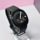 Reloj inteligente negro con pantalla redonda, mostrando la fecha 9 de marzo. Correa ajustable. Fondo blanco y rosa.