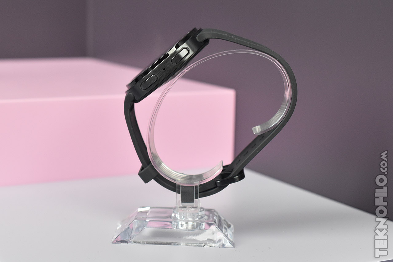 Reloj inteligente negro sobre soporte transparente con fondo rosa y gris. Tecnología y diseño moderno.