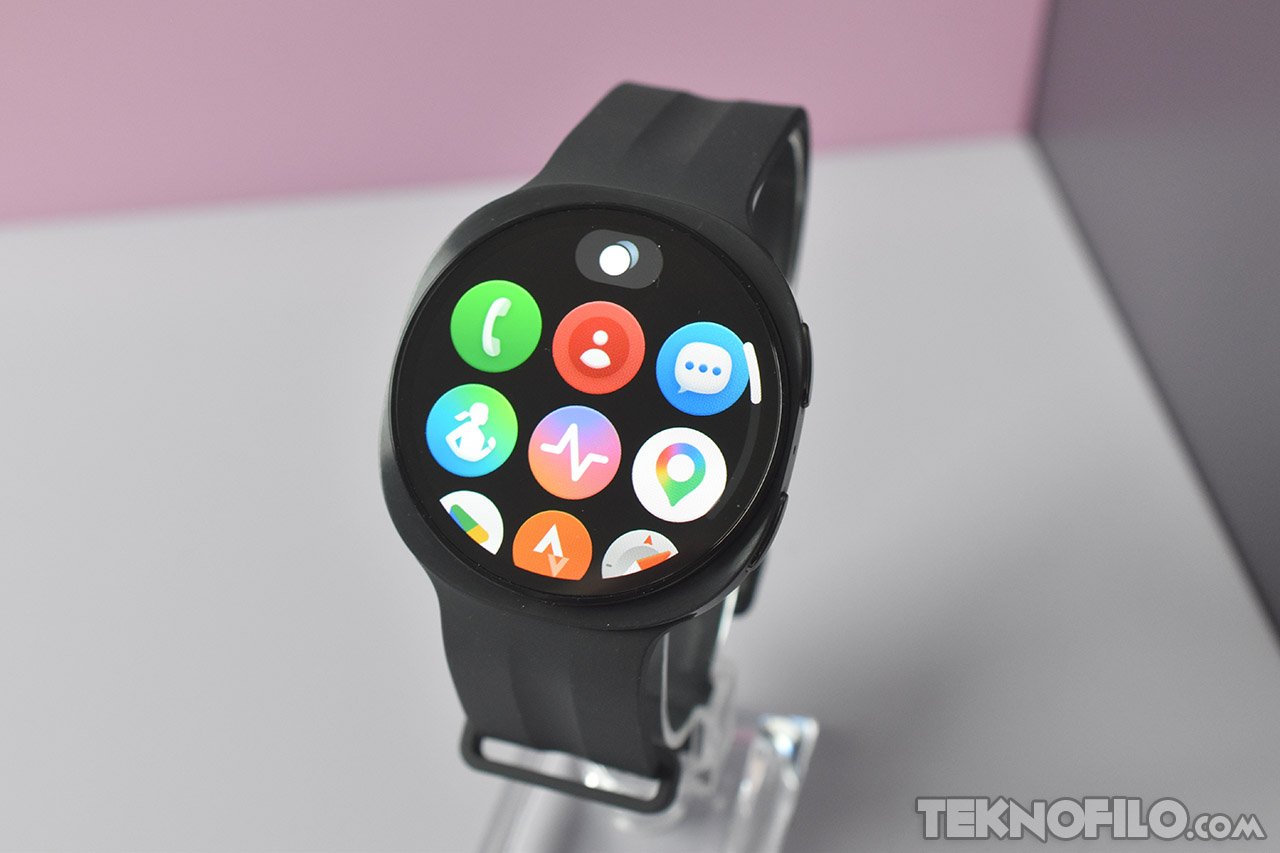 Reloj inteligente con pantalla de aplicaciones coloridas sobre un fondo rosa y blanco.