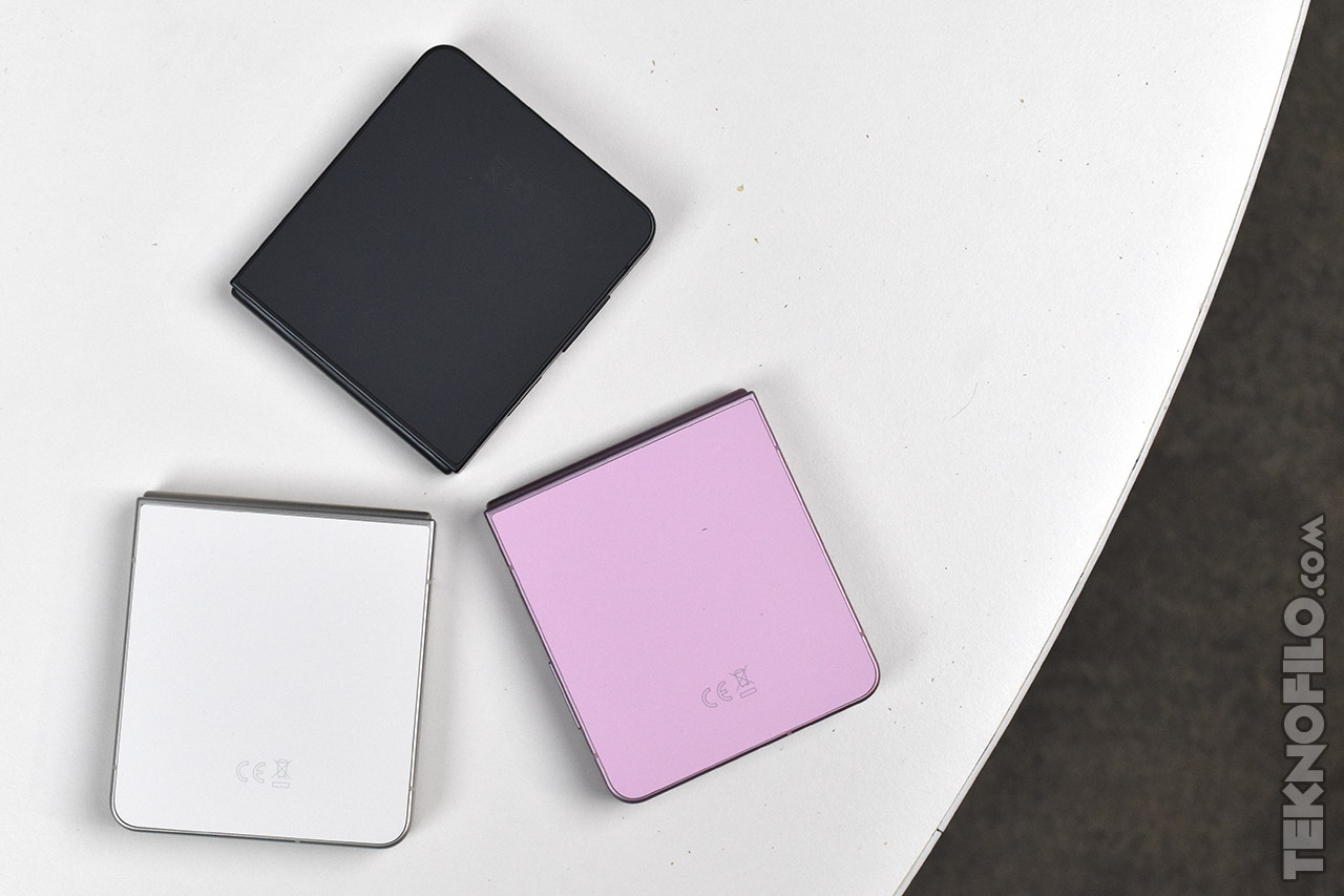 Tres teléfonos plegables en colores negro, blanco y rosa sobre una mesa blanca, vistos desde arriba.