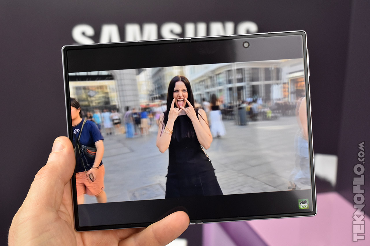 Persona sosteniendo dispositivo Samsung mostrando foto de mujer en la calle haciendo gesto divertido.