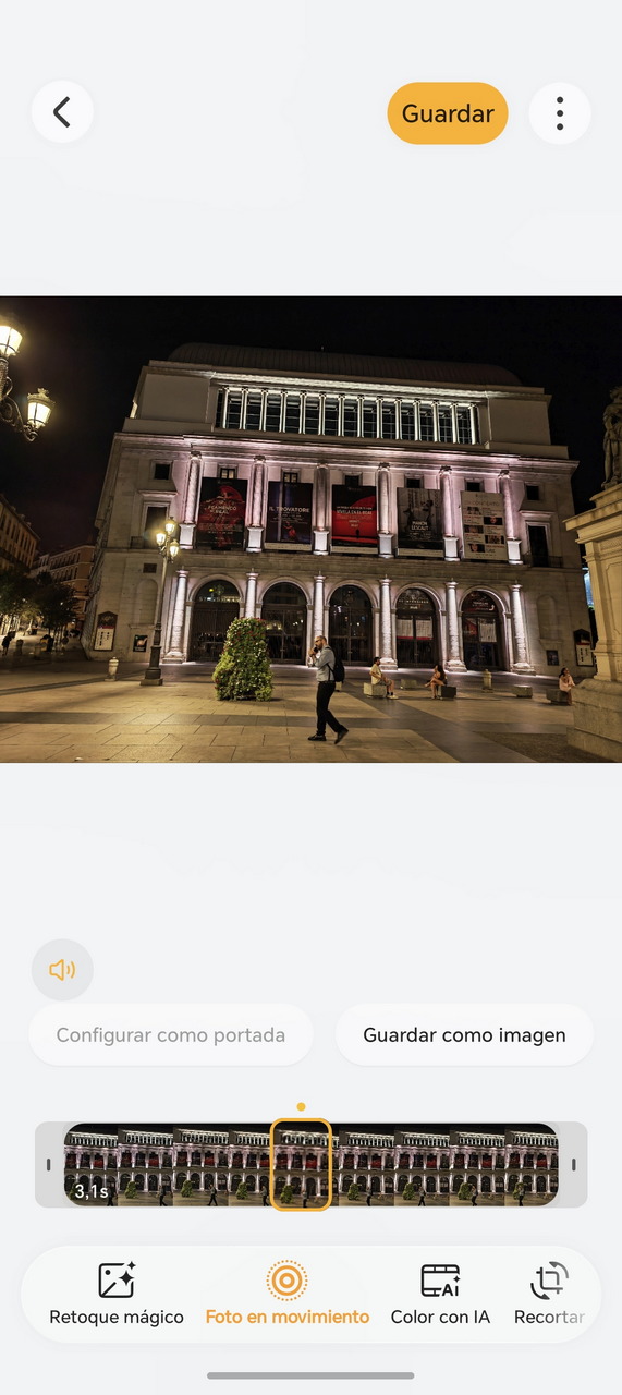 Edificio iluminado en la noche con transeúntes caminando por la plaza, frente a su fachada con carteles coloridos.