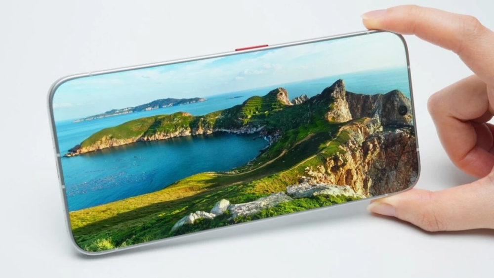 Este móvil sorprende con una pantalla que no tiene marcos Persona sosteniendo un smartphone mostrando un paisaje costero con montañas y mar, en pantalla completa.