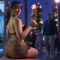 Una mujer en una fiesta al aire libre de noche, sosteniendo una copa, rodeada de personas y edificios iluminados.