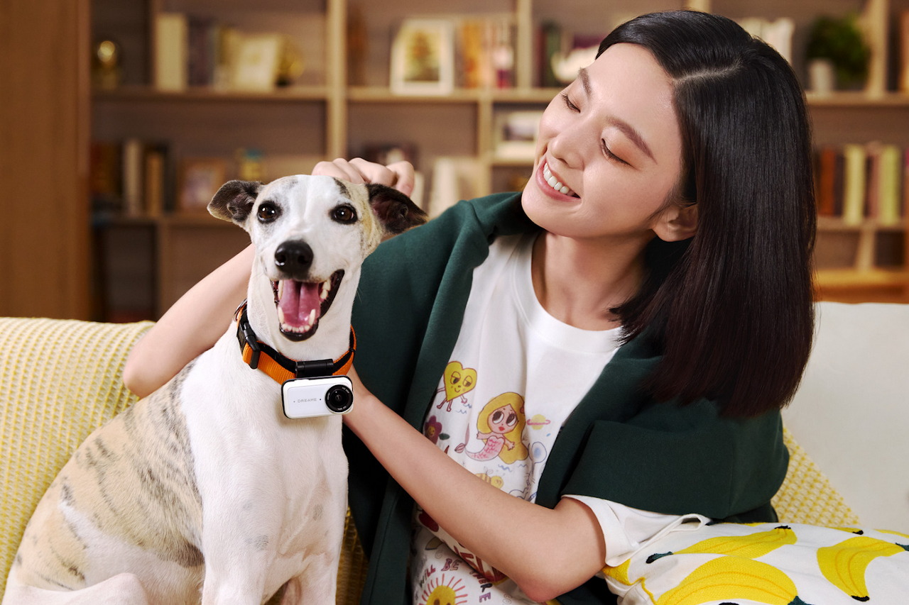 Mujer sonriente acariciando a un perro con collar inteligente en un salón acogedor. Felicidad y tecnología en casa.