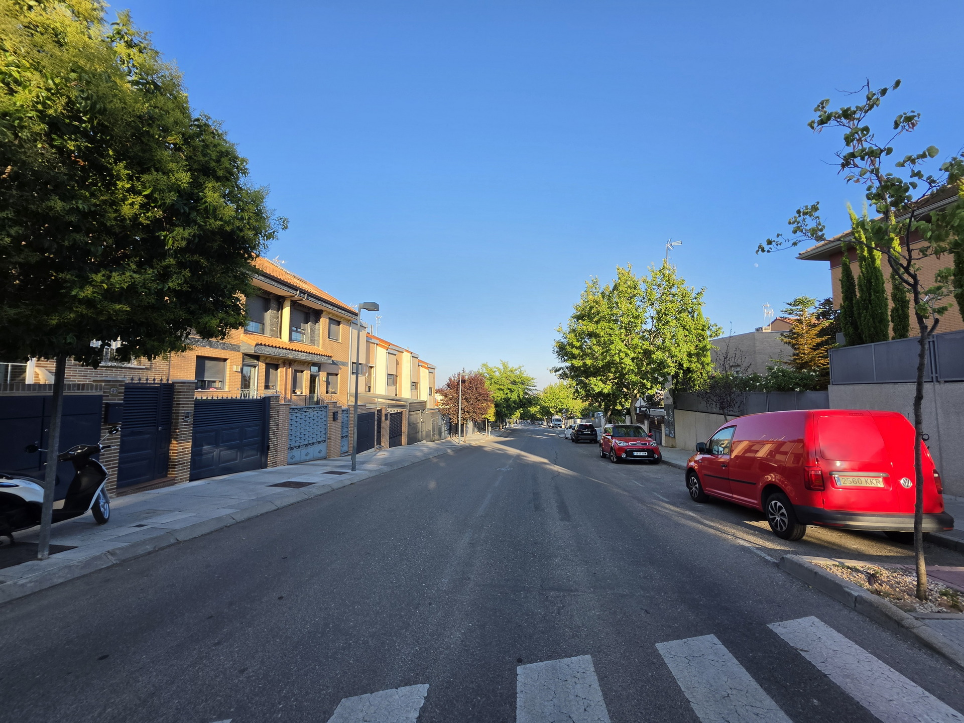 Calle residencial con casas modernas, coches estacionados y cielo azul claro. Ideal para paseos tranquilos.