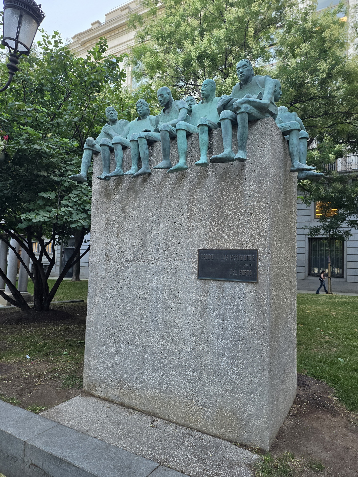 Escultura de figuras humanas en un pedestal, rodeada de árboles, en un parque de Madrid.
